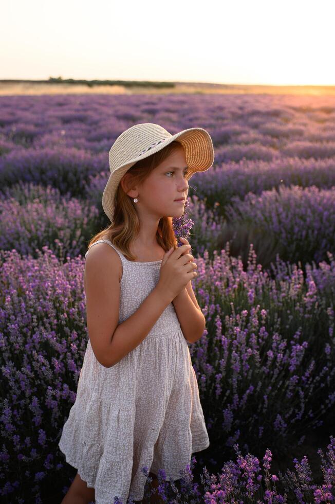 Little girl framed by purple flowers under a sky painted with orange and pink. photo