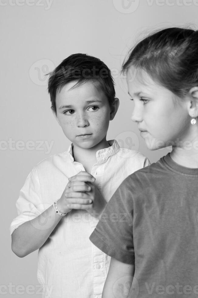 Close up black and white image of a small boy and girl facing each other, foreheads almost touching, gentle expressions, studio light highlights emotional connection. photo