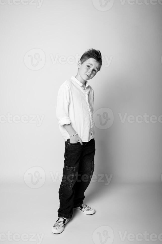 Black and white photo of a boy posing like a model, standing tall with a slight turn of the body, gaze focused forward. Studio light creates clear contrast and detail.