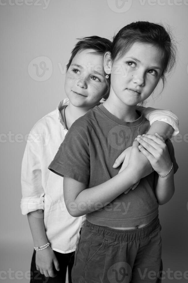 Tight black and white portrait of a young brother and sister, faces close together, looking in different directions. Studio lighting creates soft shadows and emotional depth. photo