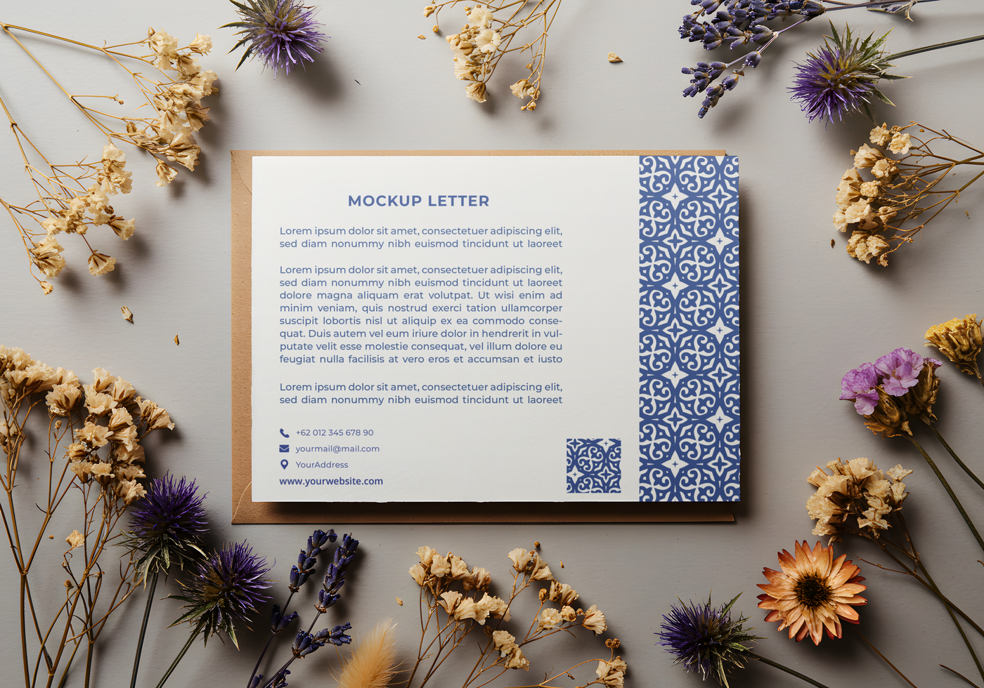 A mockup letter with a blue patterned border rests on a gray surface surrounded by dried flowers psd