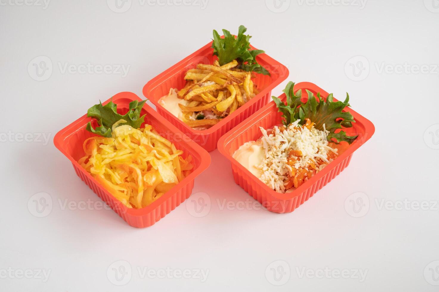 Three red plastic containers holding an assortment of salads and fries with garnishes, for takeaway or ready-to-eat meals. photo