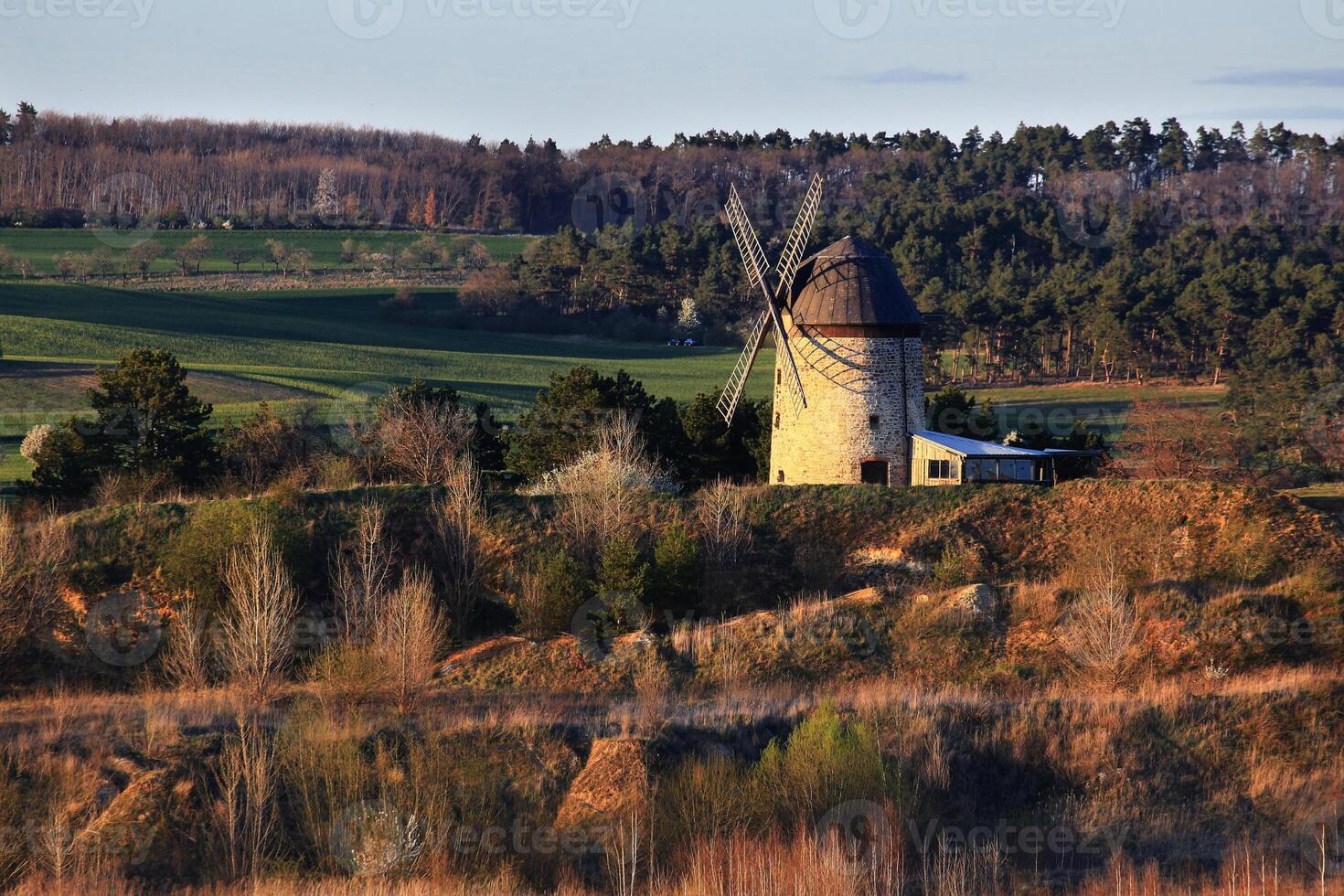 Stone windmill sitting on a gentle slope surrounded by trees in warm evening light photo