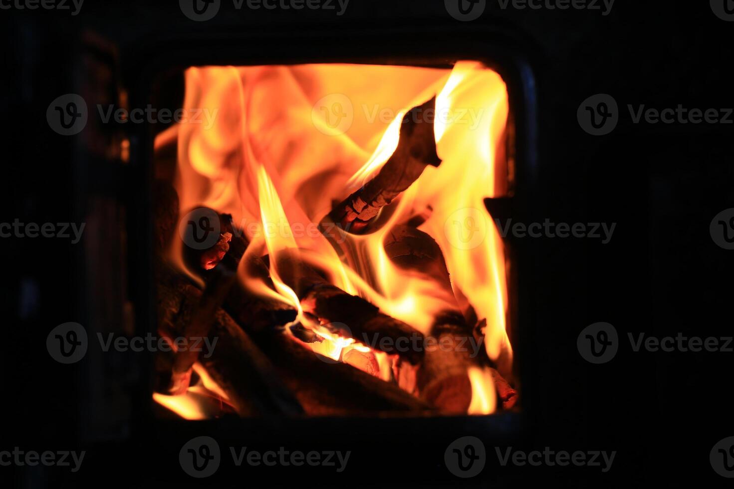 Close-up of intense flames and wood burning inside dark iron stove with visible inner firebox photo