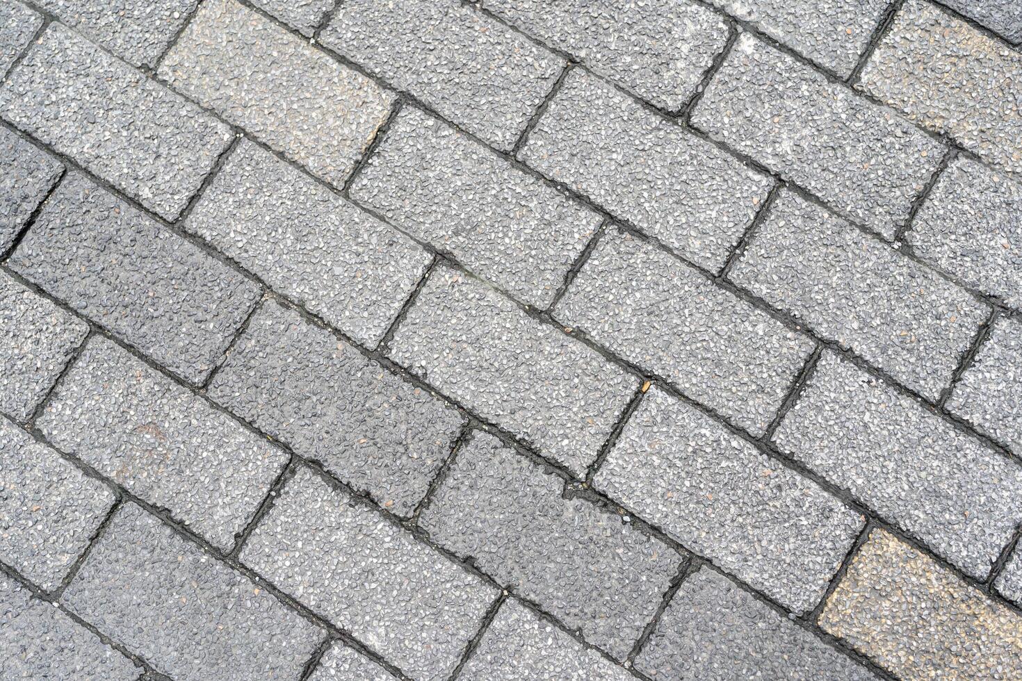 Textured grey paving stones laid in a diagonal pattern, creating a durable and classic outdoor surface. The rough texture and varying shades of grey provide a natural and sturdy backdrop. photo
