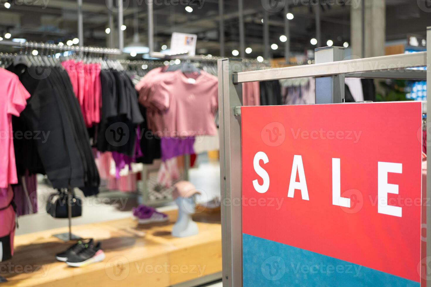 Red Sale Sign in Clothing Store. discounts and promotions on apparel. Racks of various clothes are visible in the background. shopping discounts, consumerism and promotions. photo