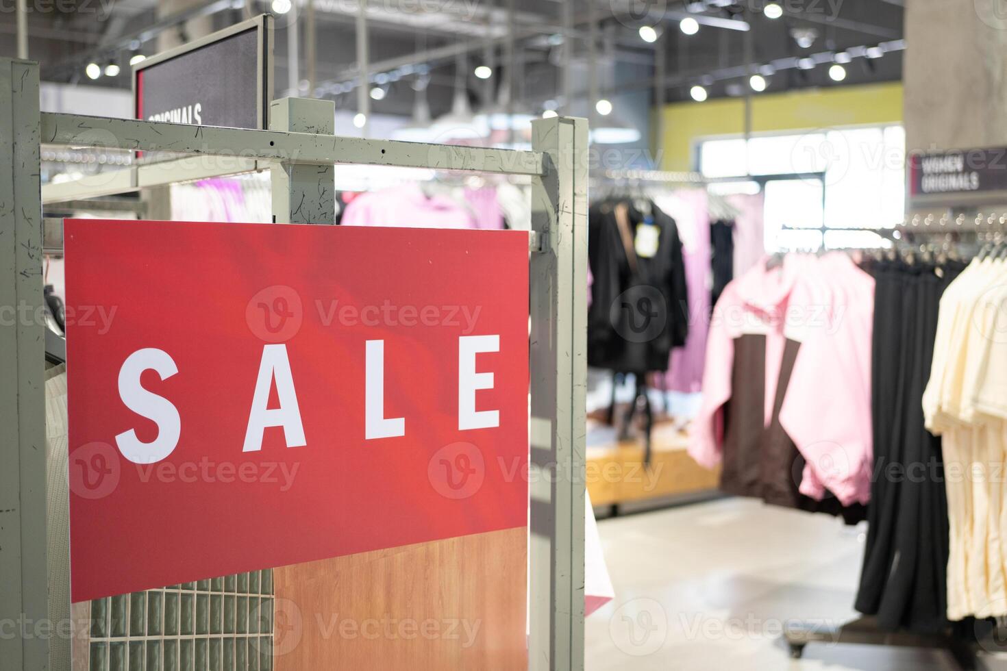 Red Sale Sign in Clothing Store. discounts and promotions on apparel. Racks of various clothes are visible in the background. shopping discounts, consumerism. photo