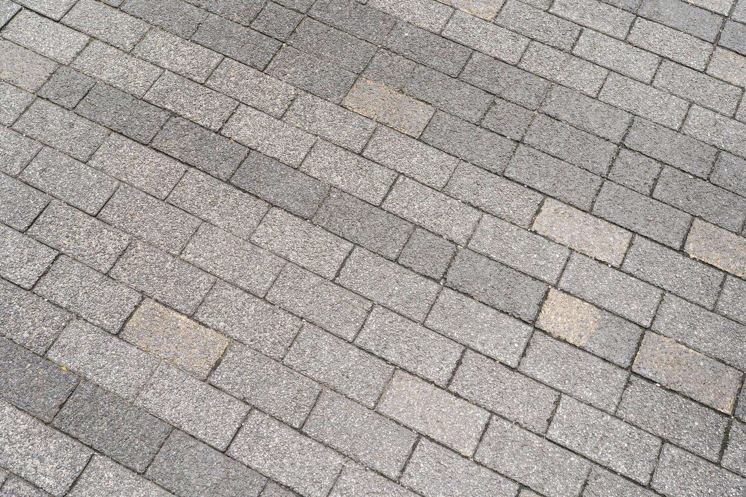 Textured grey paving stones laid in a diagonal pattern, creating a durable and classic outdoor surface. The rough texture and varying shades of grey. photo