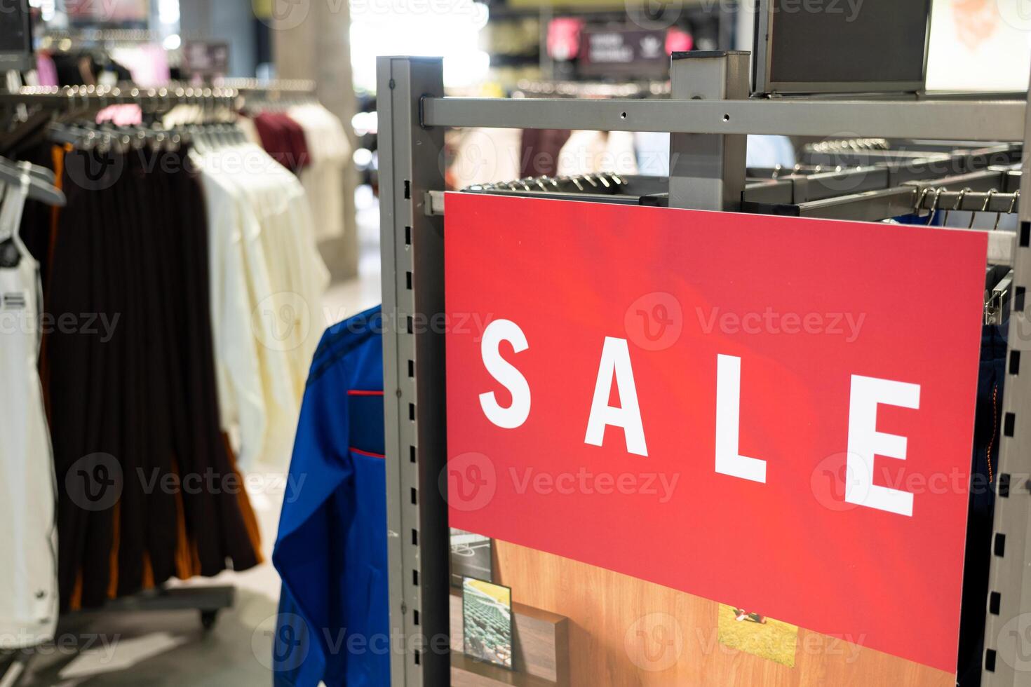 Red Sale Sign in Clothing Store. discounts and promotions on apparel. Racks of various clothes are visible in the background. shopping discounts, consumerism, and fashion promotions. photo