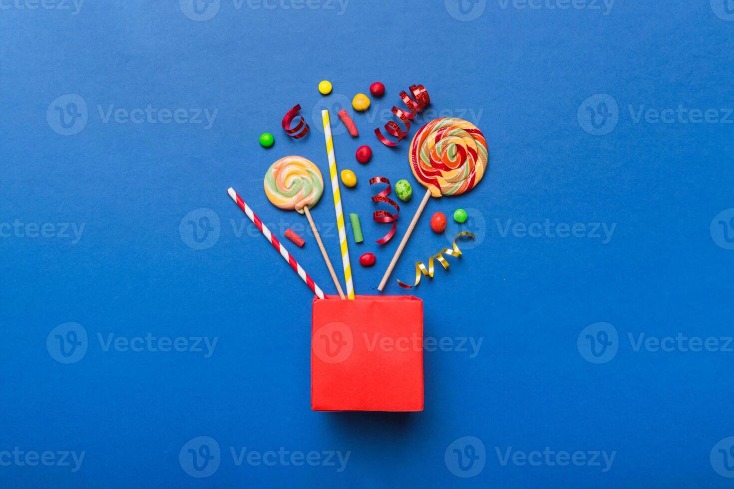 gift box in corner full assorted candies falling out on colored background photo