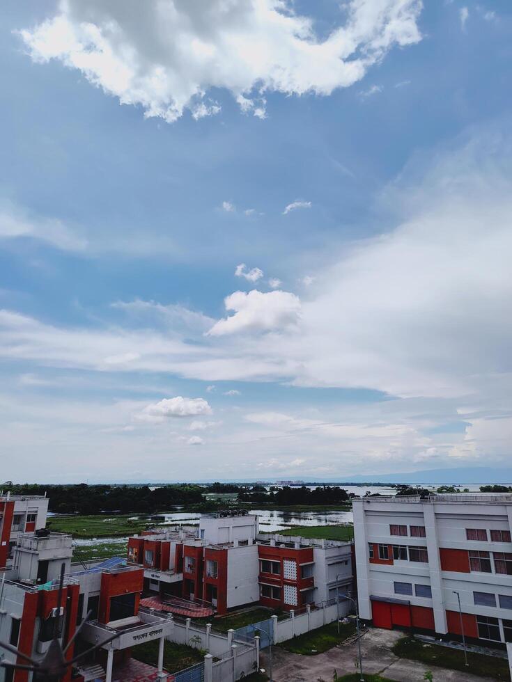 Aerial view of urban buildings with red and white facades merging into green fields and a river beneath a partly cloudy sky. Ideal for cityscape, nature, and landscape themes. photo