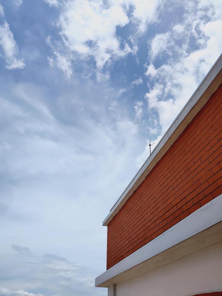 Low angle shot of red brick building corner with white trim against a blue sky and scattered clouds. Strong architectural lines and contrast. Ideal for urban and design themes. photo
