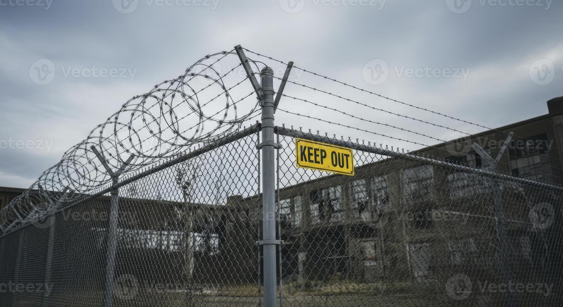 Security fence with razor wire and keep out sign at abandoned building photo