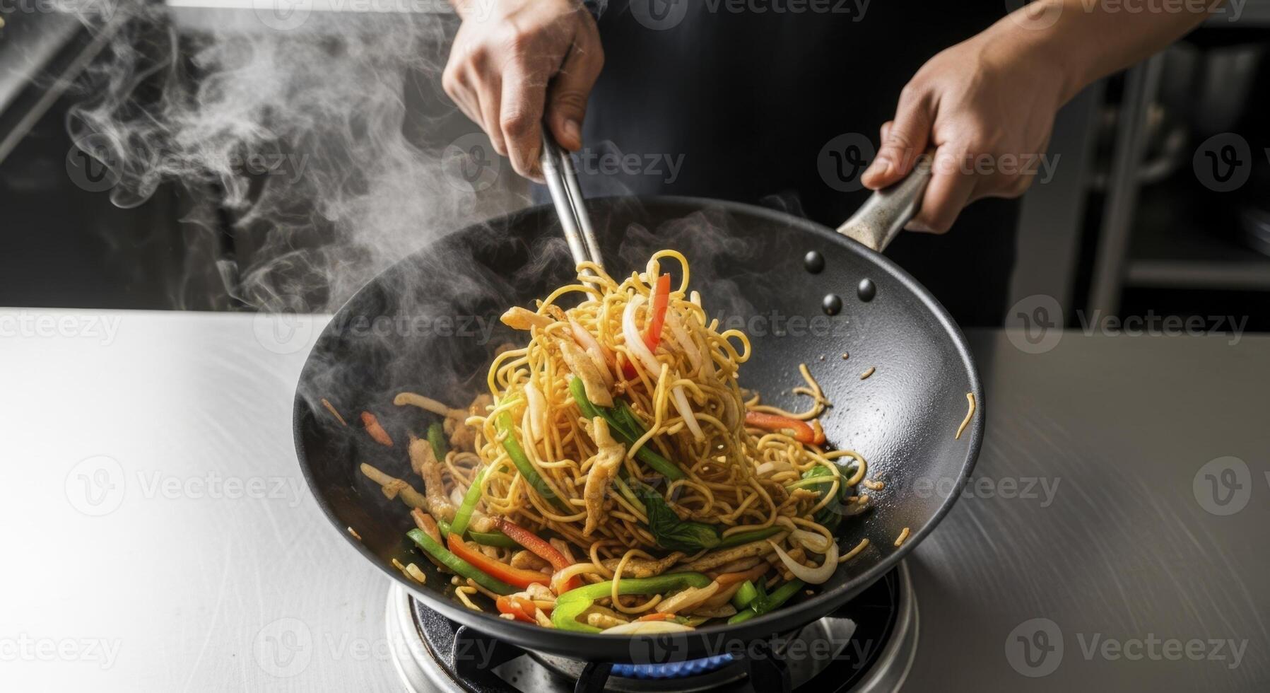 Chef hands tossing steaming vegetable stir fry noodles in a hot wok on a stove photo