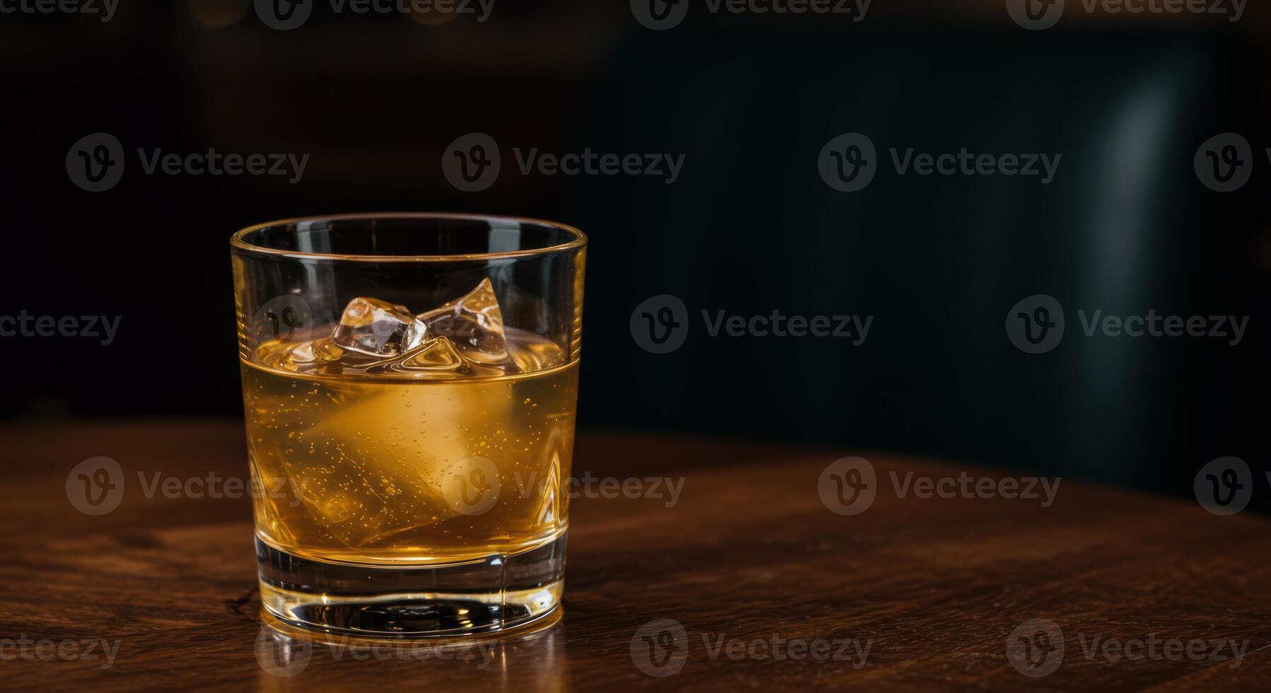A glass of whisky with ice cubes rests on a wood table offering a sophisticated drink concept for menus and promotions photo