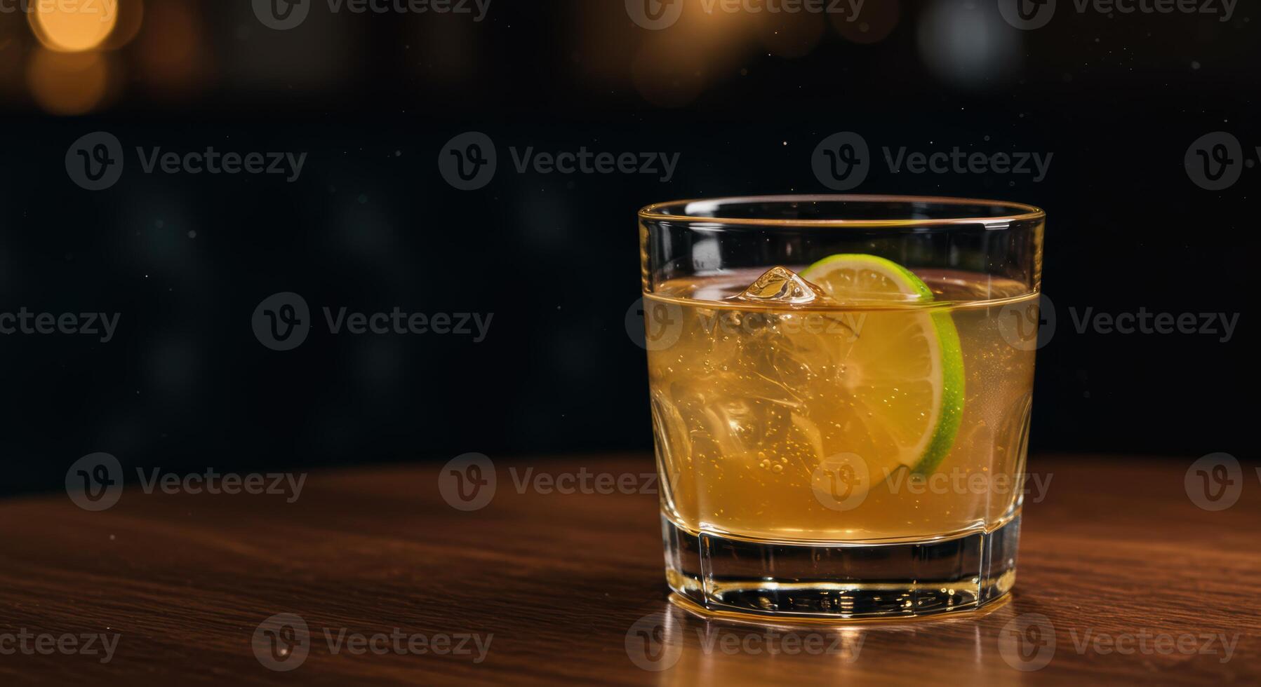 Delicious golden cocktail with ice and a lime slice sitting on a beautiful wooden surface photo
