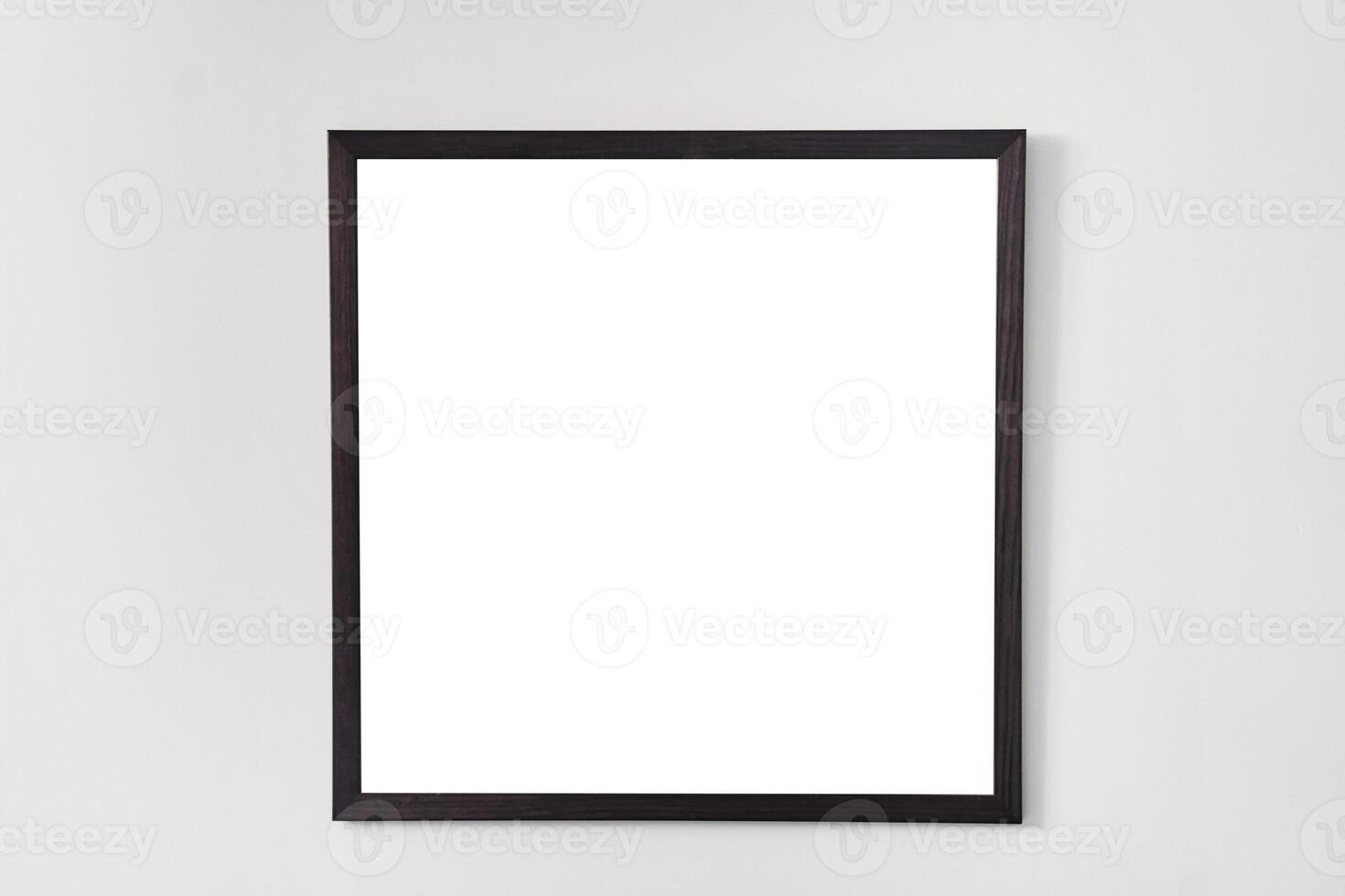 An empty square photo frame with a black border hanging on a white wall
