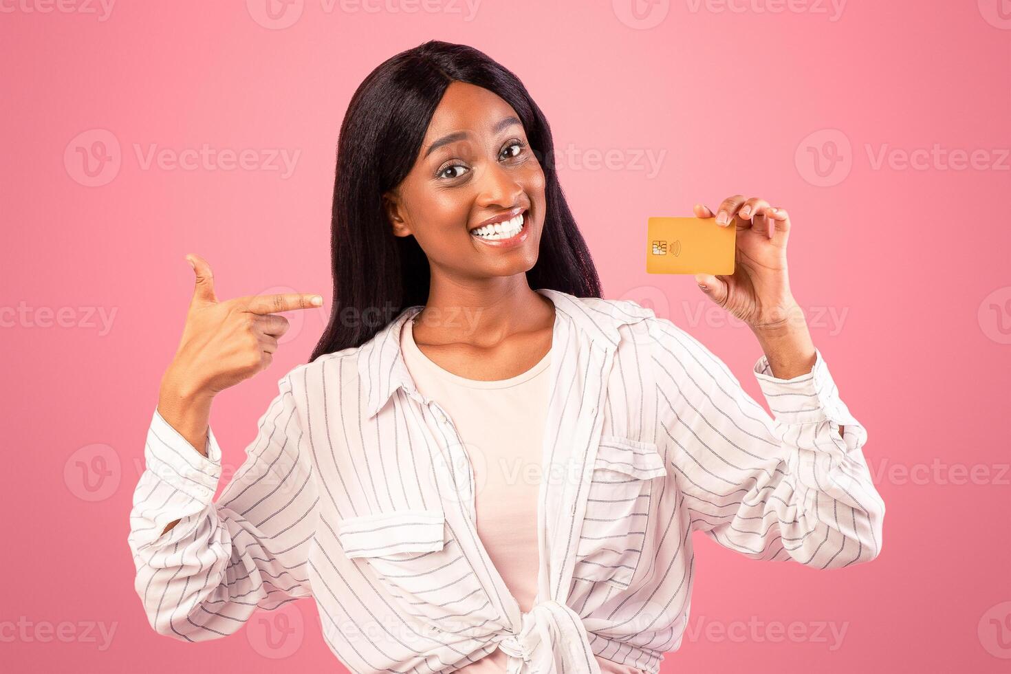 Contactless shopping concept. Joyful black woman pointing at credit card with smile on pink studio background. Portrait of charming African American lady recommending bank services photo