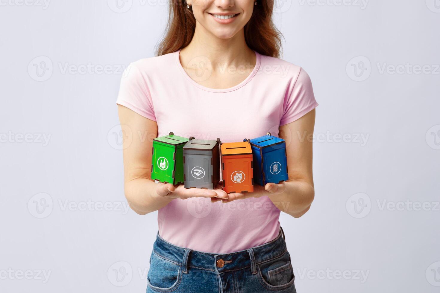Concept Image For Waste Sorting With Young Woman Holding Different Colorful Toy Garbage Containers For Different Kind Of Trash, Standing Over Gray Background In Studio, Cropped Image, Closeup photo