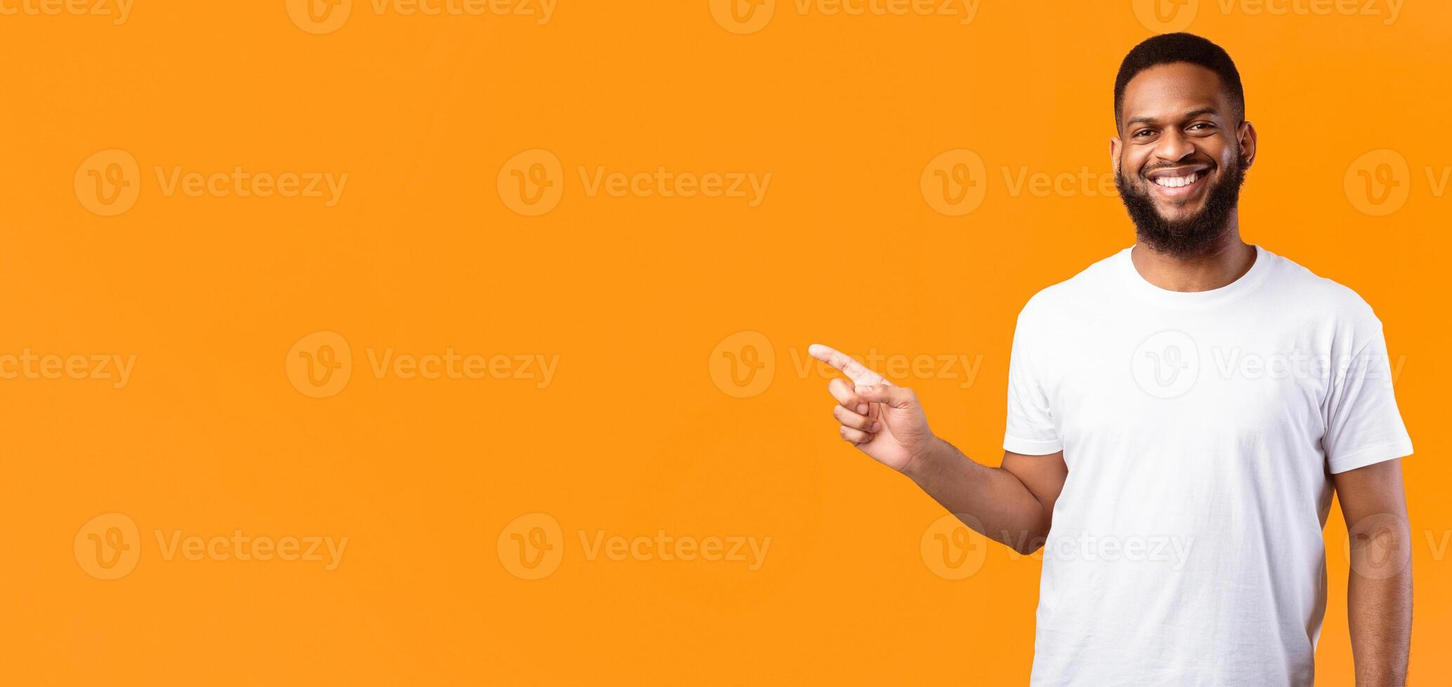 Black Man Pointing Finger Aside Advertising Your Text Standing Posing Smiling To Camera Over Yellow Studio Background. Look There, Advertisement Banner Concept. Empty Space For Text photo