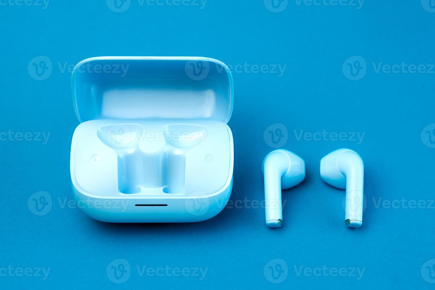 A pair of modern wireless earbuds placed next to an open charging case on a blue background. A sleek, stylish, and compact audio accessory perfect for daily use, music, and calls. photo