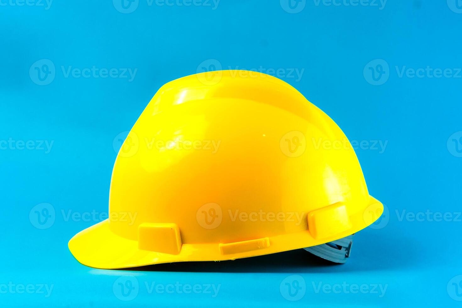 Bright yellow construction hard hat on a blue background. Safety helmet for industrial workers, engineers, and builders, symbolizing workplace protection and occupational safety. photo