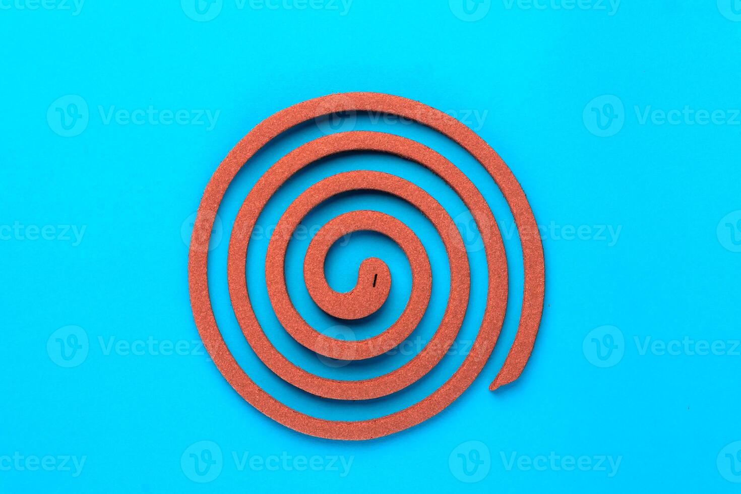 A single brown mosquito coil in a spiral shape on a blue background. Traditional insect repellent used for mosquito control, providing protection for indoor and outdoor environments. photo