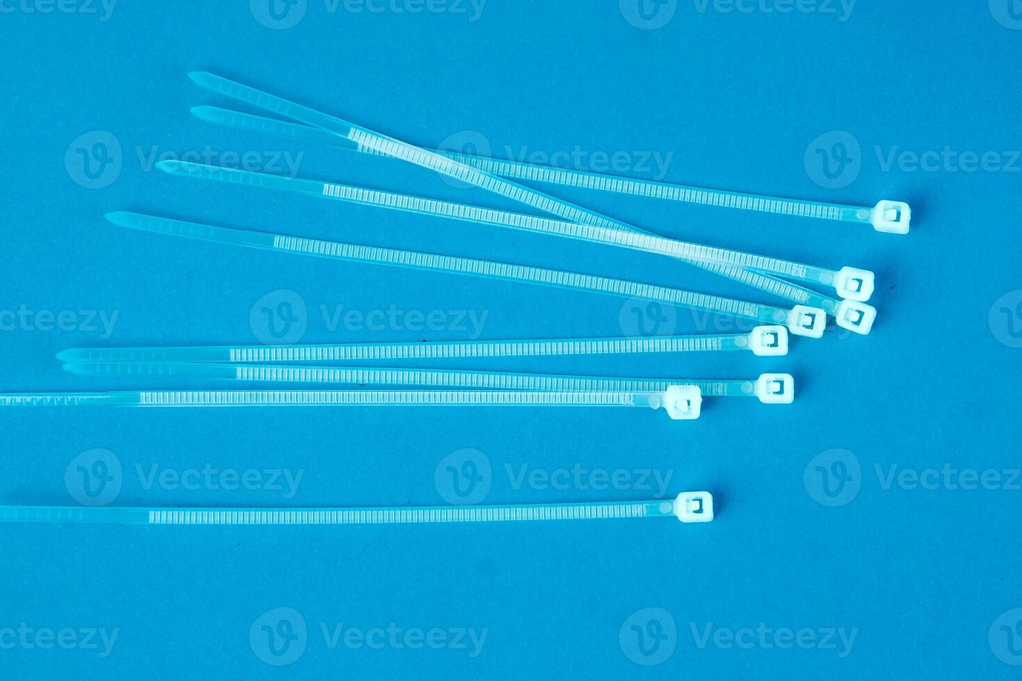 A set of transparent plastic cable ties arranged on a bright blue background. These zip ties are commonly used for organizing wires, securing objects, and bundling cables efficiently. photo