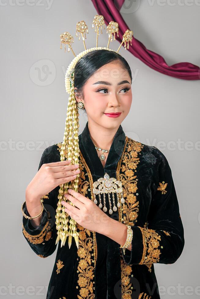 Beautiful young Asian woman smiling softly while wearing traditional Javanese bridal attire, with elegant makeup, intricate accessories, and graceful facial expression in studio shot. photo