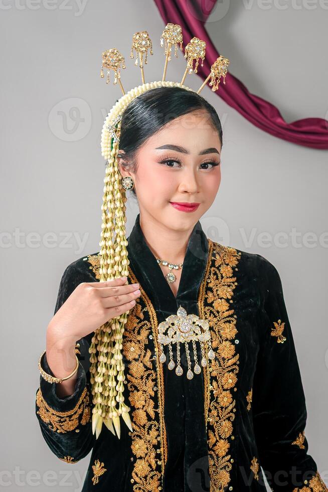 Woman smiling confidently while wearing traditional Javanese wedding attire, with elegant makeup and intricate accessories, captured in a graceful studio portrait. photo