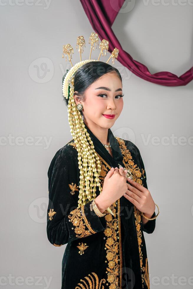 Charming Asian woman smiling subtly in traditional Javanese attire, showcasing elegance and pride through her poised expression, detailed makeup, and cultural accessories. photo