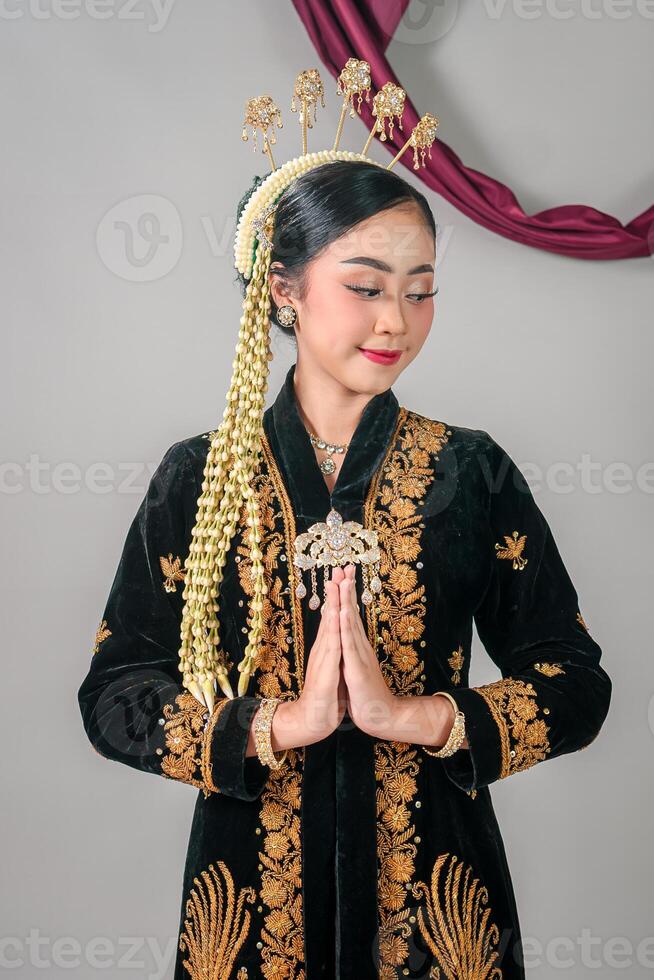 Asian woman in traditional Javanese attire smiling gently with graceful hand gesture. Her serene expression and cultural outfit reflect elegance and heritage proudly photo