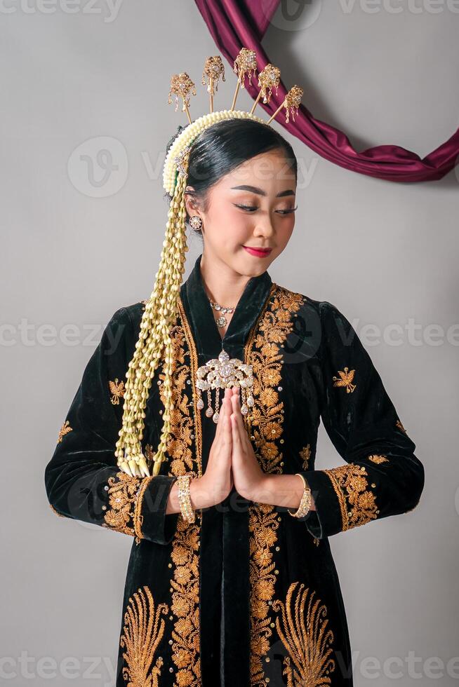Asian woman in traditional Javanese attire smiling gently with graceful hand gesture. Her serene expression and cultural outfit reflect elegance and heritage proudly. photo