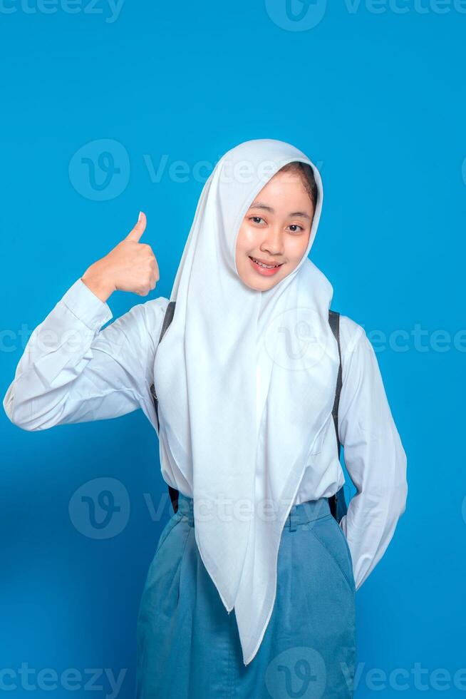Confident Muslim schoolgirl wearing hijab and uniform giving a thumbs up with a warm smile. Her bright expression conveys optimism, positivity, and encouragement in education. photo