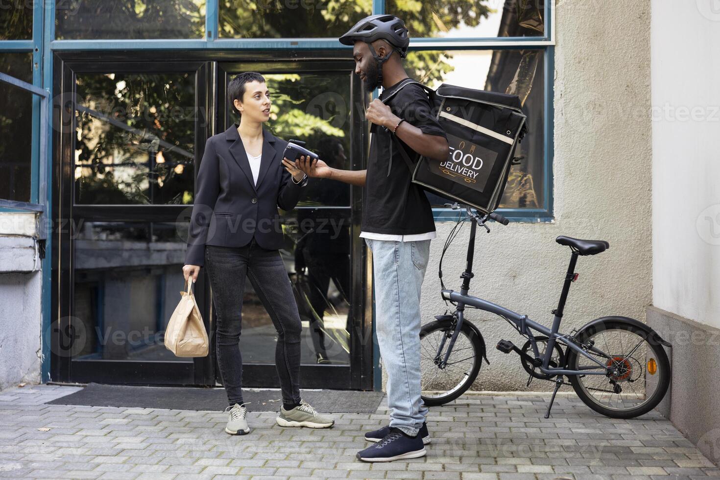 Black delivery person completes a food transaction as customer pays with smartphone. The quick service interaction takes place during a city service drop off at her doorstep. photo