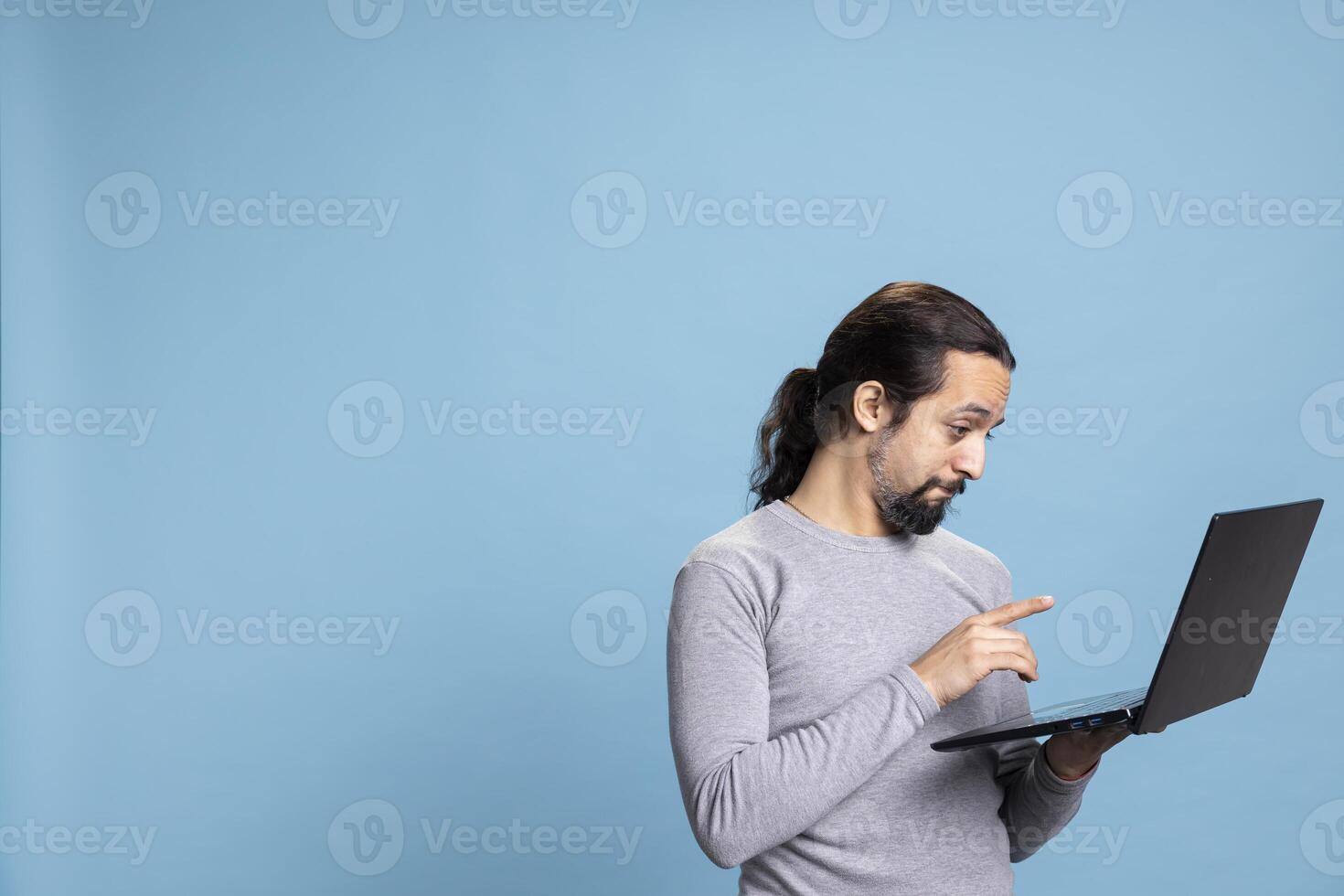 Cheerful and focused young person using his pc for online tasks, embodying the concept of digital connectivity. Man with long hair browsing the web for modern work or internet communication. photo