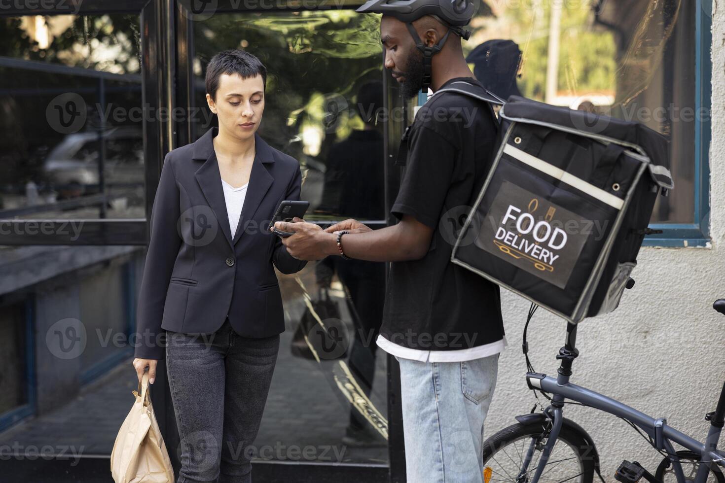Delivery worker with backpack receives payment from woman for a meal order. The contactless nfc transaction with the smartphone reflects the modern online buying process for takeout services. photo
