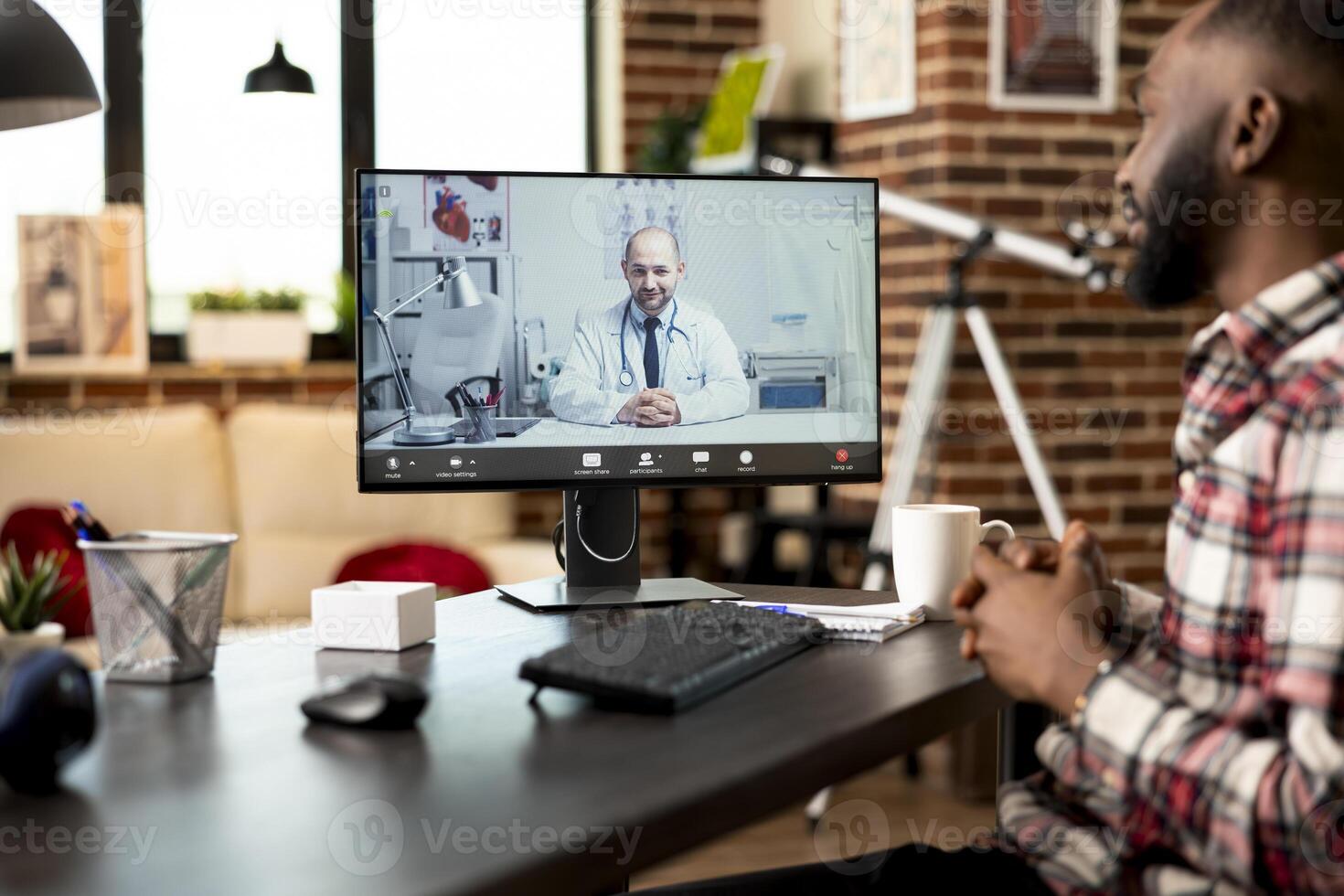 Black male employee seated at desk working remotely, describes symptoms during virtual consultation with caucasian doctor. Professionals discuss telemedicine project from home office via call. photo