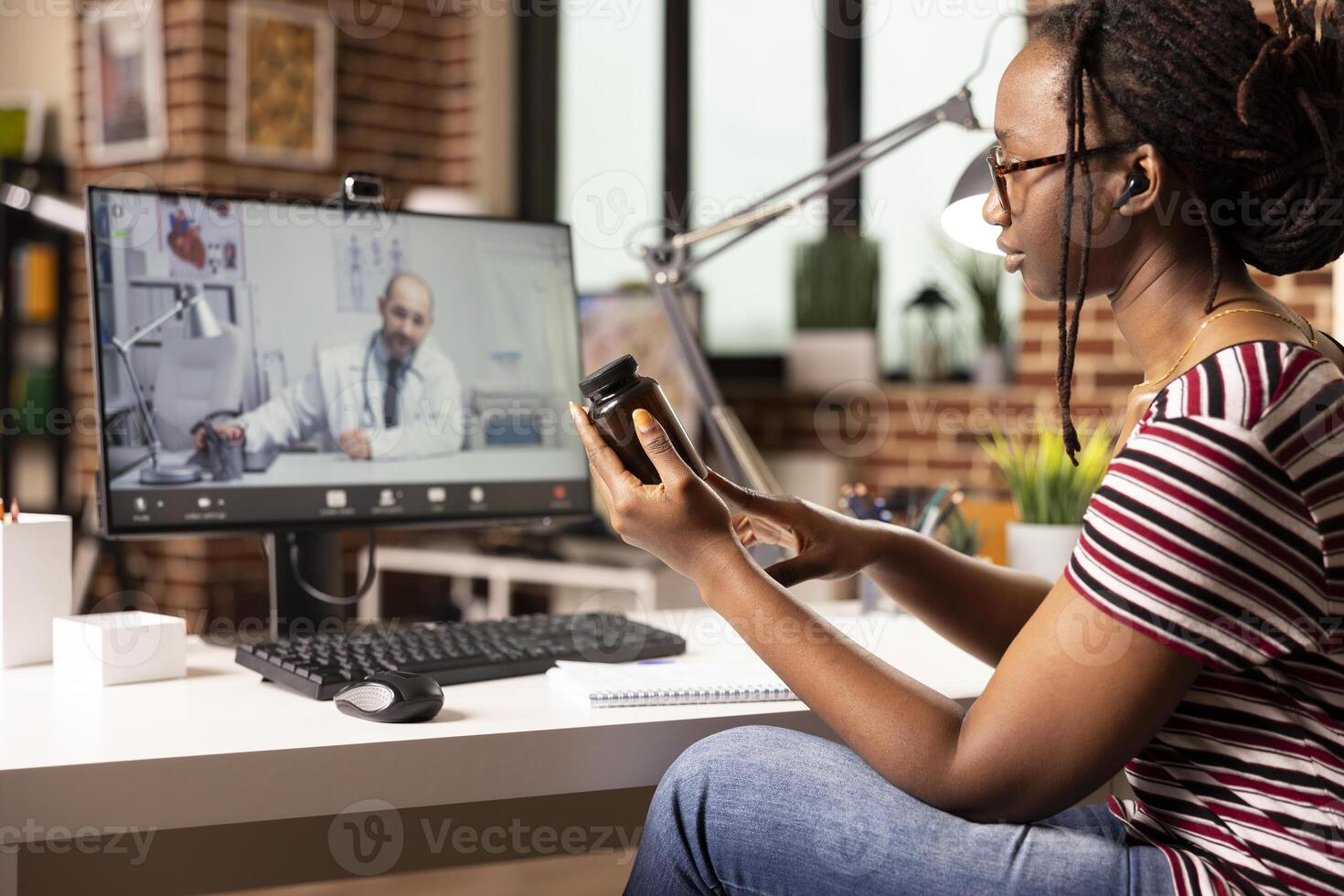 African american woman sitting at home desk having online medical consultation on desktop pc. Black female patient discusses prescription pills with doctor during virtual telemedicine appointment. photo