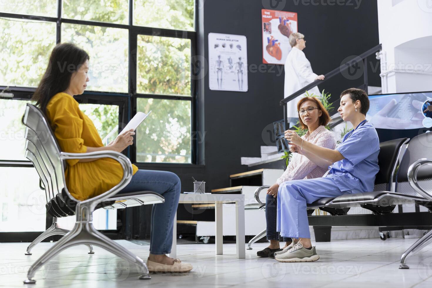 Female nurse offers advice and a clear explanation of x ray image to a patient during a health check in a hospital lobby. Specialist analyzes radiology scans for a recovery plan. photo