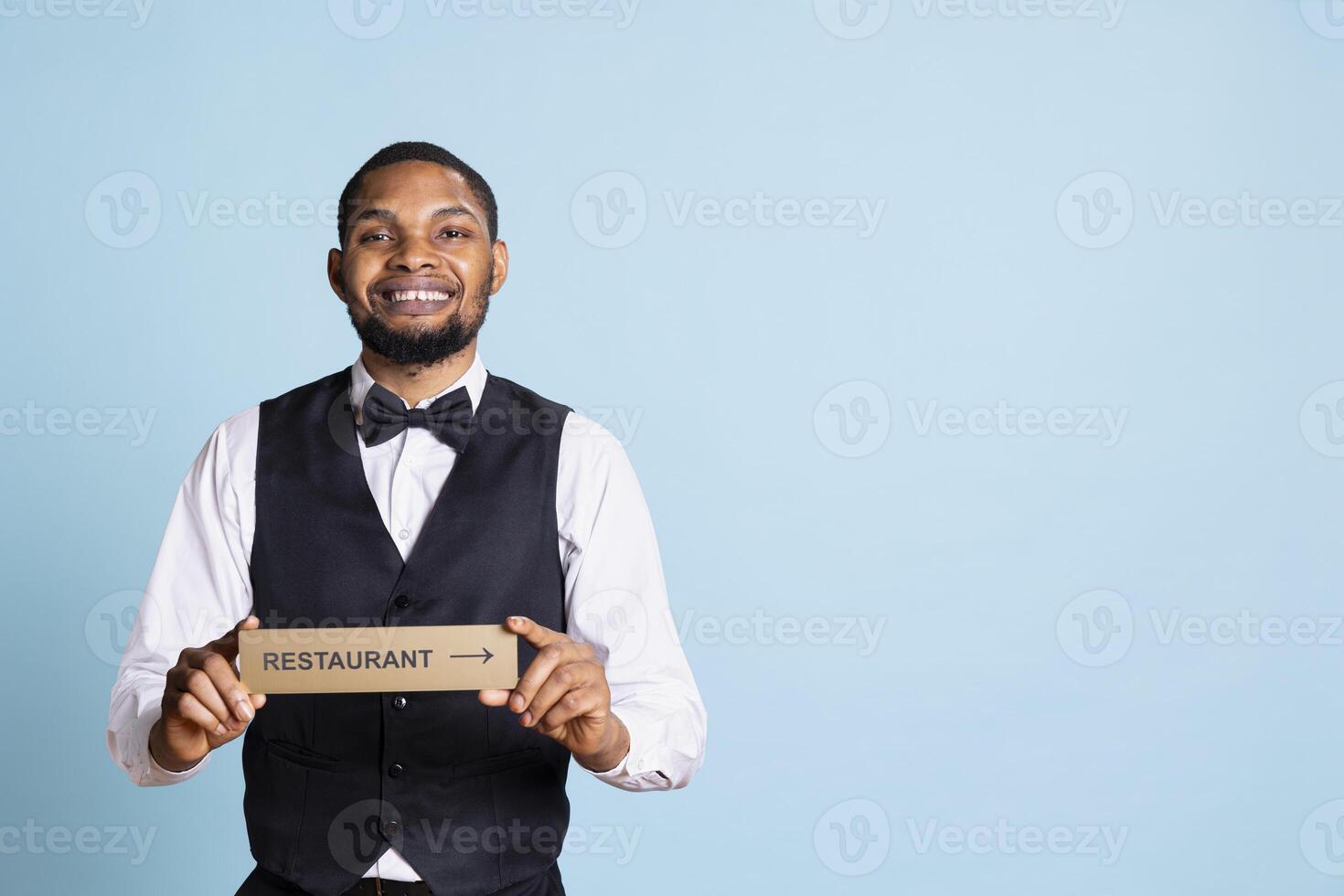 Doorman bellhop showing the restaurant direction with a hotel sign, holding an indicator to point guests to the amenities. Professional hotel concierge in suit and tie using a wall mark. photo