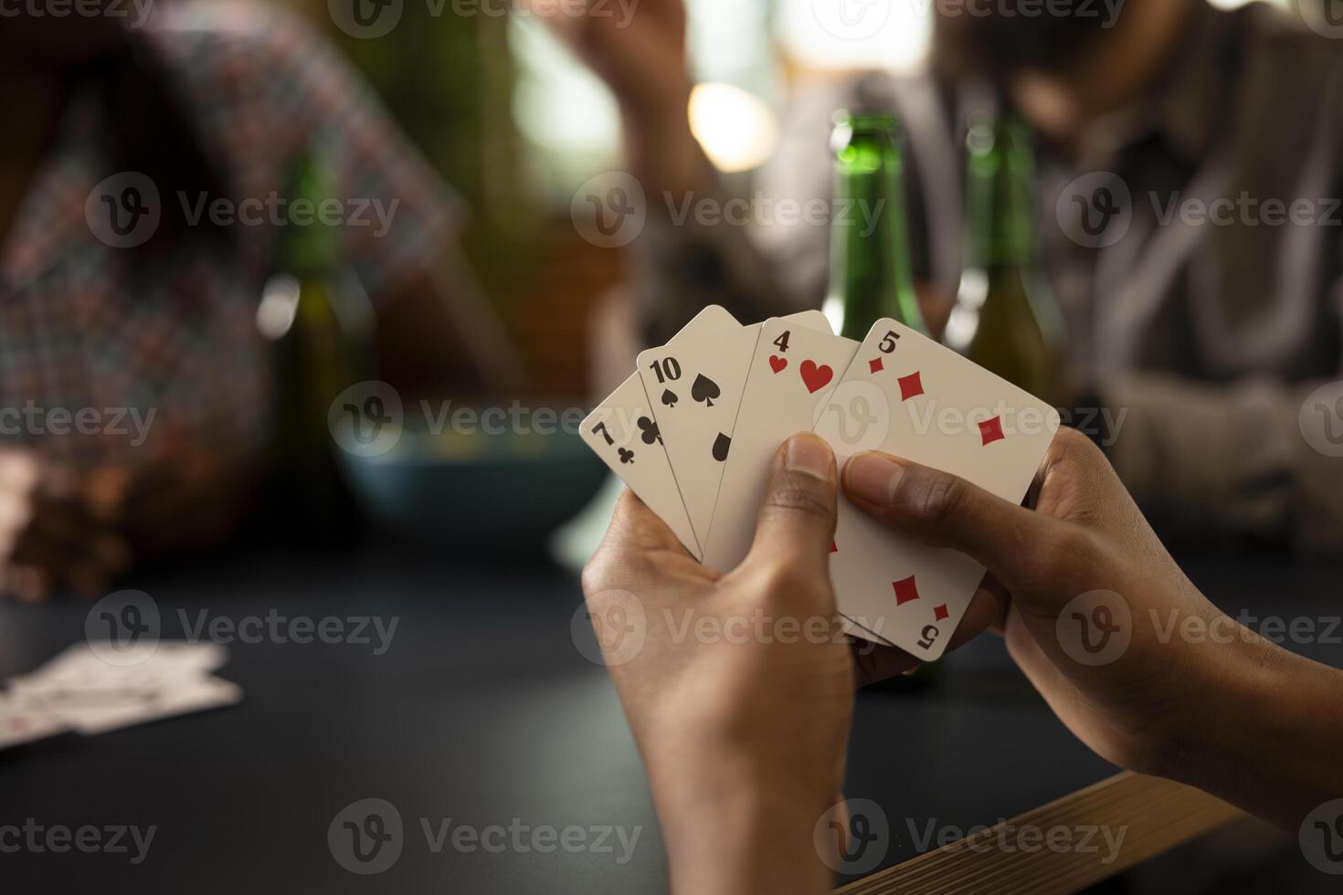 Closeup of african american hand gripping playing cards during fun indoor activity with friends, surrounded by snacks and refreshments. Black person holding pair of cards during casual gaming session. photo
