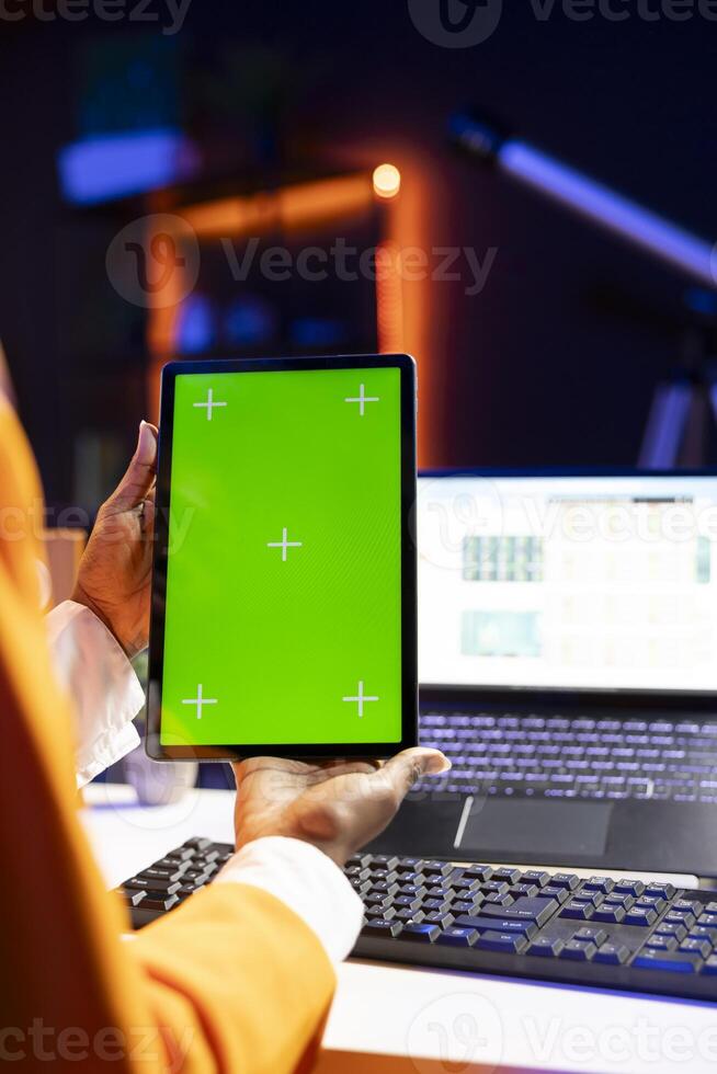 Self employed person at home checks statistics on laptop while using chroma key tablet. Remote worker holding isolated screen device, analyzing business graphics, close up shot photo
