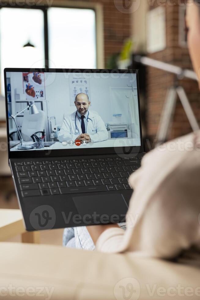 Female individual sitting at home having online medical consultation on laptop. Self employed woman talks to family doctor, seeking health advice during virtual healthcare appointment. photo