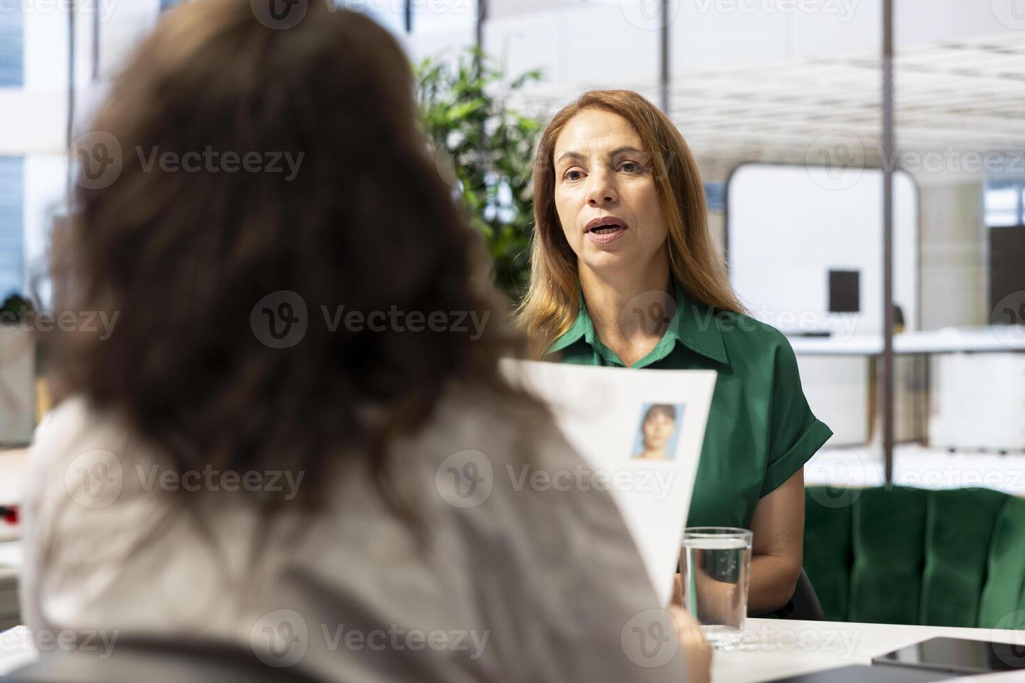 Recruiter hiring for newly opened company position, looking over applicant CV, having discussion with her. HR worker looking over candidate resume, identifying skills fitting job posting photo