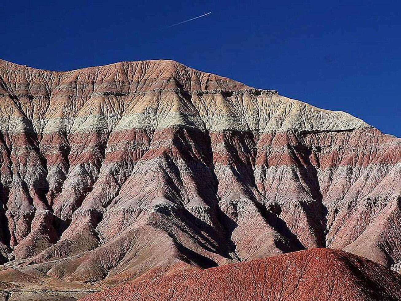 A Desert Mountain's Ancient Layers Unveiled Under a Vast Blue Sky with Contrail photo