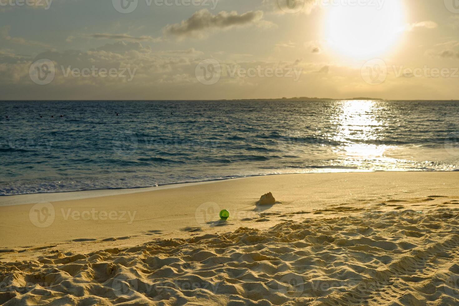 A bucket left behind from building sandcastles at sunrise in the Bahamas, and the sunlight makes the sand look golden. photo