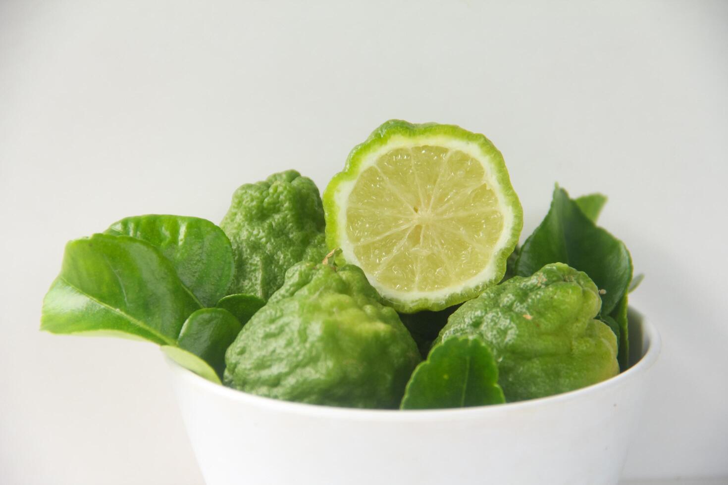 A white bowl with some lime leaves and a lime photo