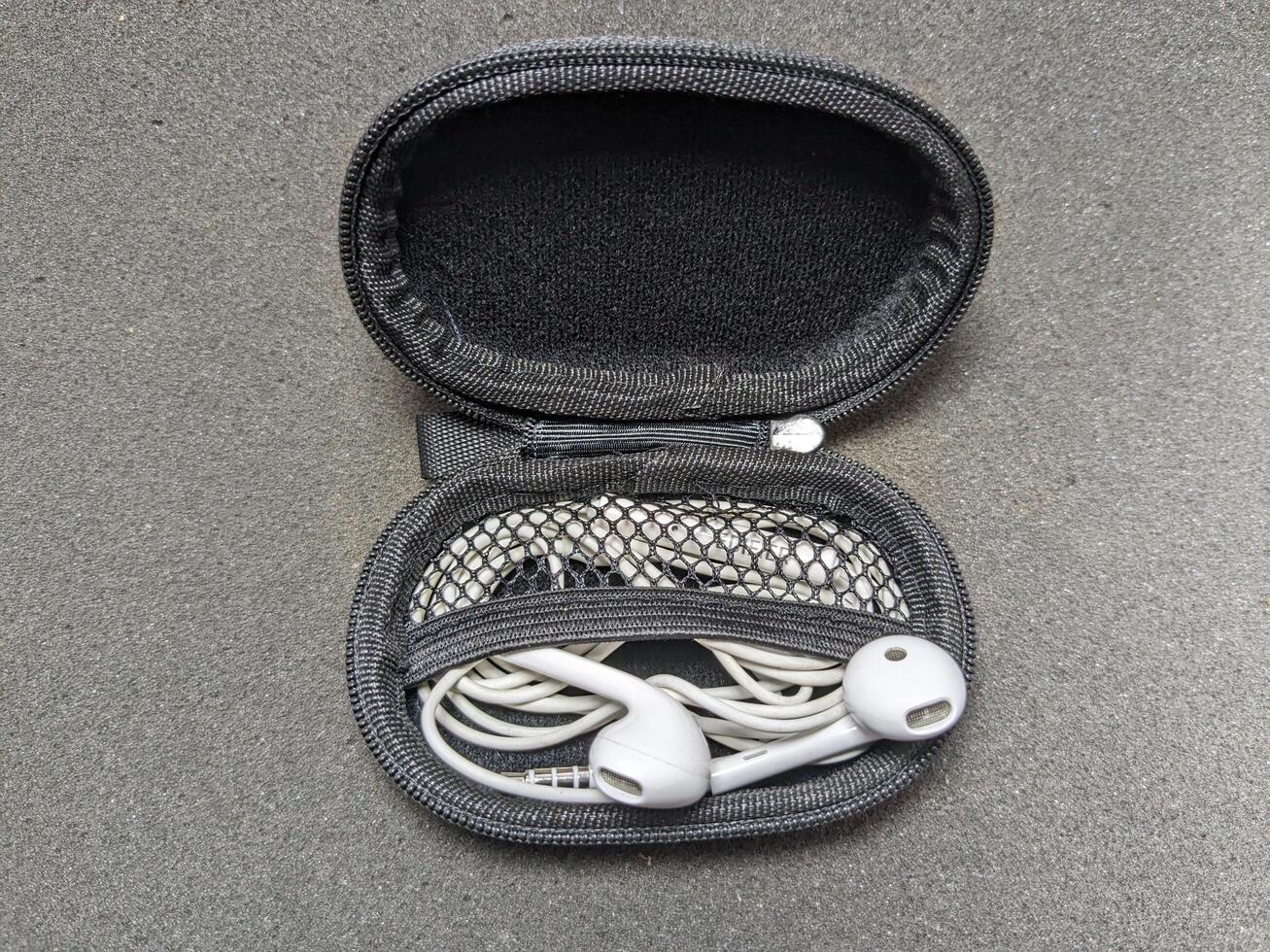 Open Earphone Case with White Wired Headphones on a Gray Textured Surface photo