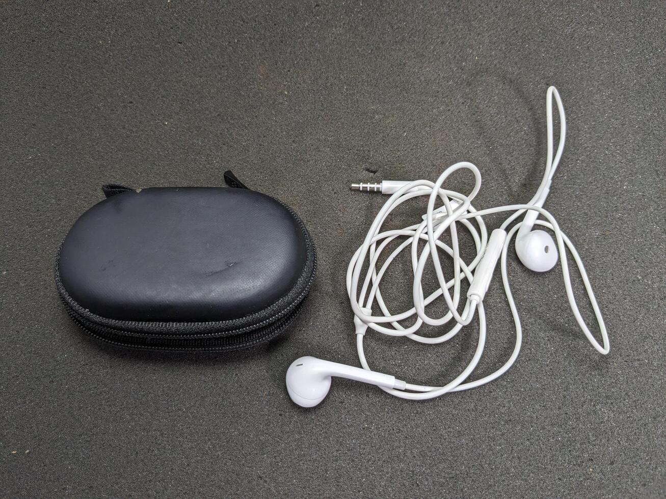 Overhead shot of white earbuds with tangled wire next to a black carrying case photo